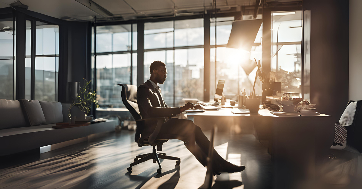 Business professional working at a modern office desk with sunlight streaming through large windows