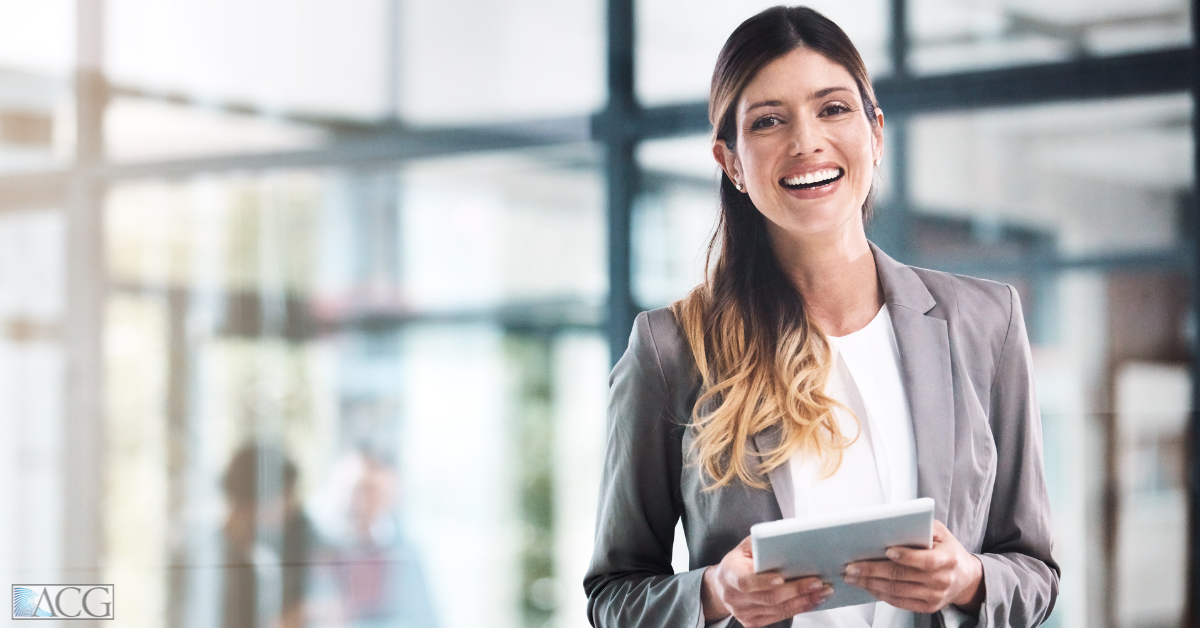 A woman is smiling while holding an iPad in an office setting.