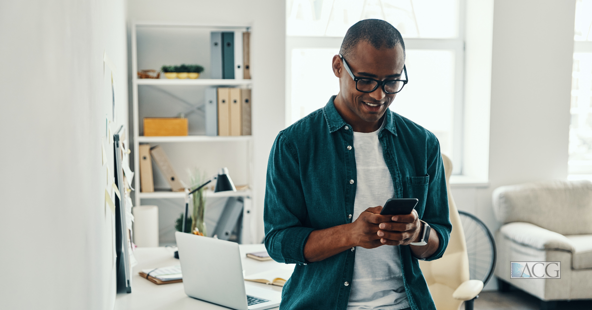 A young man looks at his mobile phone while standing in his home office.