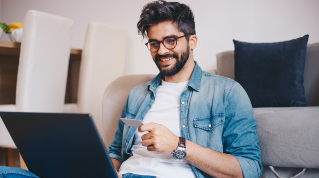 A man is sitting on his couch buying goods on his laptop.