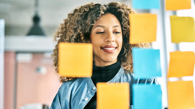 A woman is working to map out a strategy with sticky notes on a glass wall.