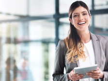 A woman is smiling while holding an iPad in an office setting.