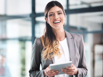 A woman is smiling while holding an iPad in an office setting.