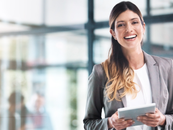 A woman is smiling while holding an iPad in an office setting.