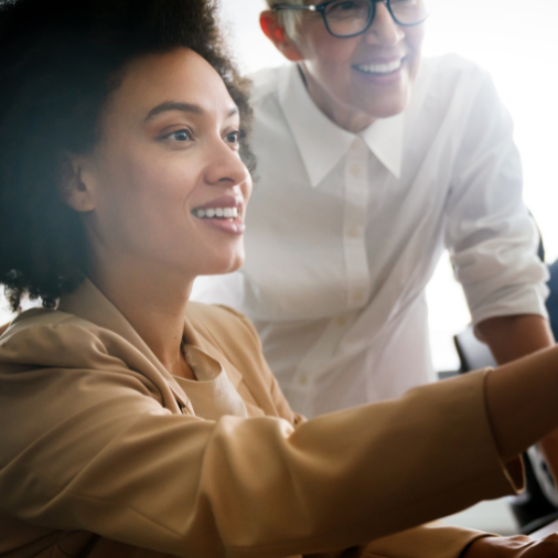 Two women smiling and collaborating on an Adobe Implementation in a modern office environment.