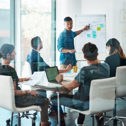 A team leader presenting ideas on a whiteboard during a meeting with colleagues.