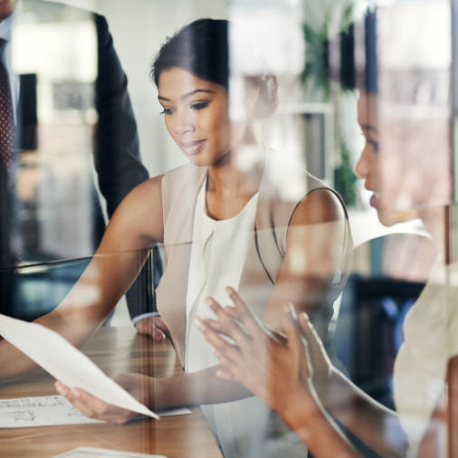 Businesswoman analyzing documents during a team meeting through a glass wall.