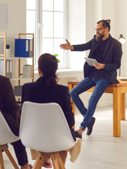 A bearded presenter gesturing during a Customized Adobe Tool Training with a small group of professionals.