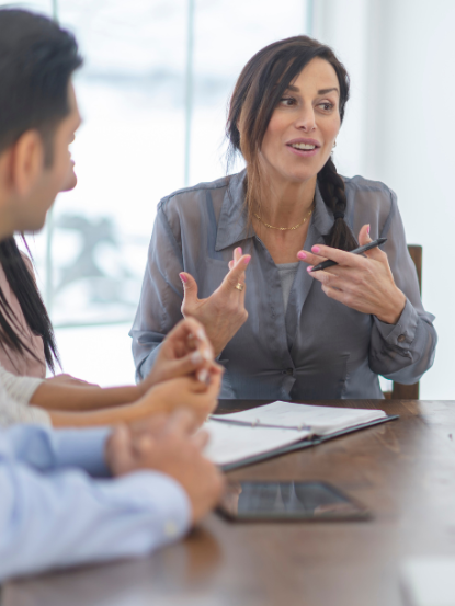 A businesswoman speaking and leading a discussion during a meeting with colleagues around a table.