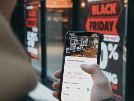 A man checks deals on his phone for a Black Friday Sale while looking at a store.